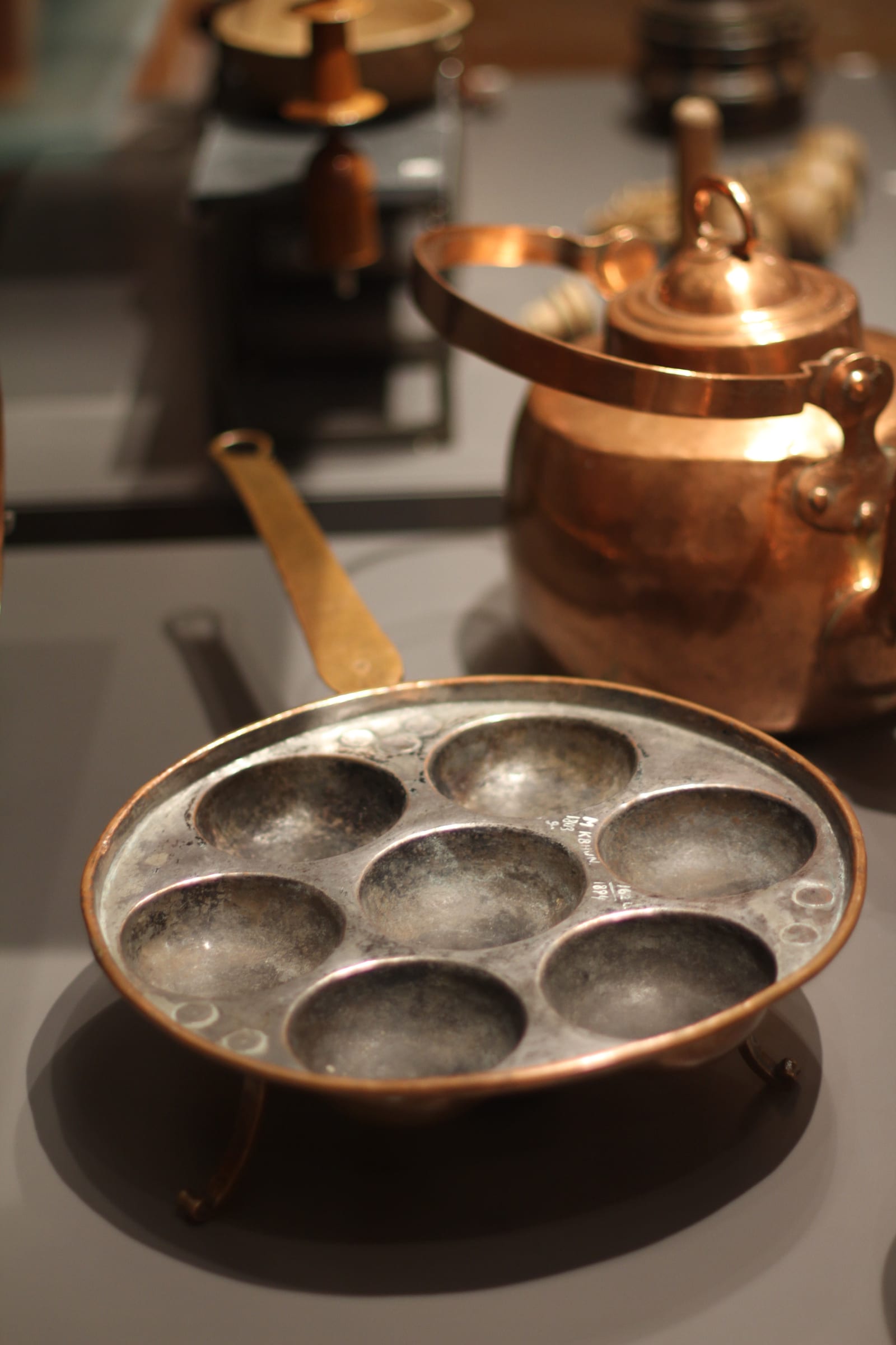 A dark cast-iron aebleskiver pan with seven deep round wells displayed at the National Museum of Denmark.