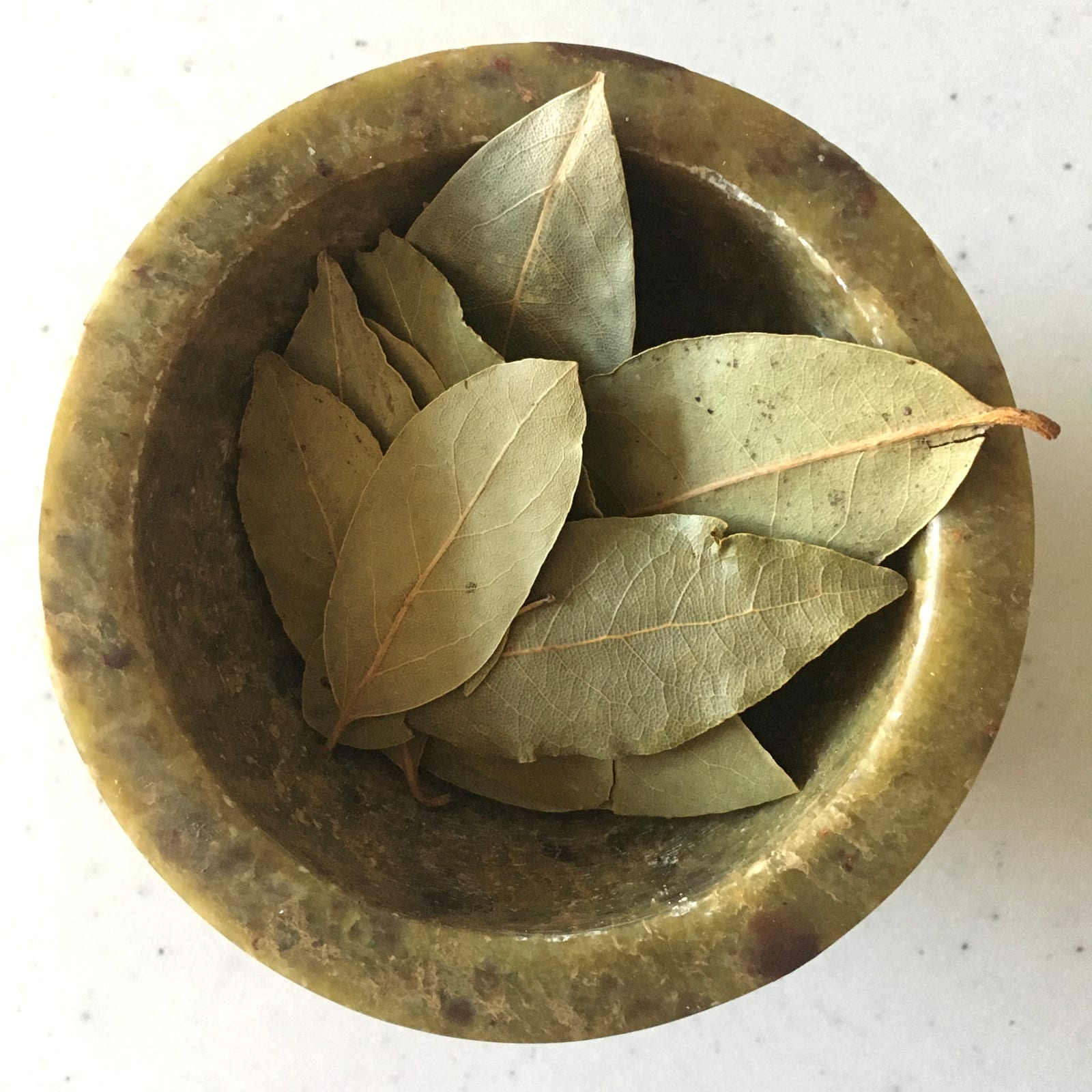 Whole dried bay leaves gathered in a round brass bowl.