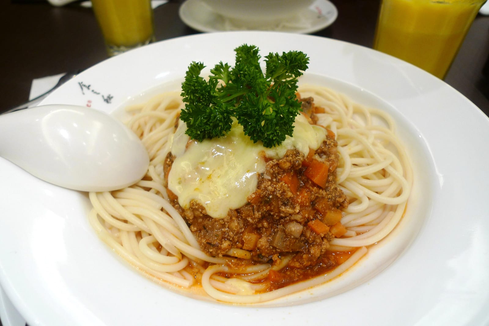 A plate of spaghetti topped with chunky meat sauce, melted cheese, parsley, and onion.