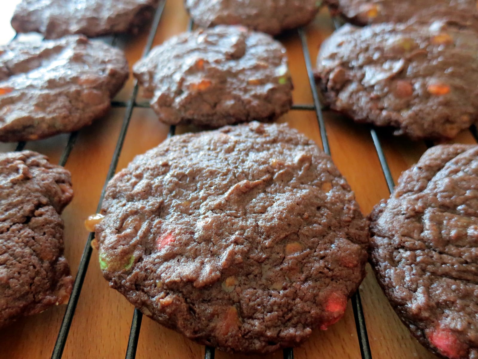 Dark double-chocolate cookies cooling close together on a black wire rack.