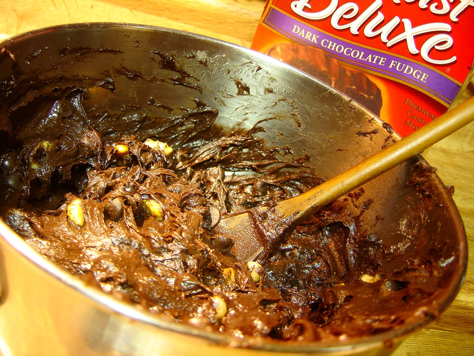 Thick dark chocolate cake-mix batter in a metal bowl with a wooden spoon and a Devil’s Food mix box behind it.