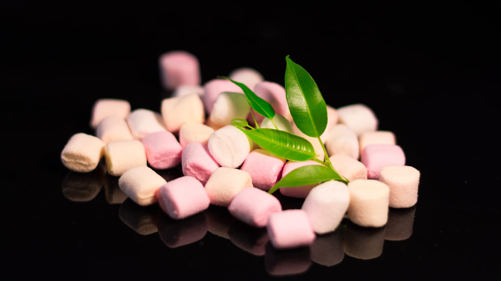 Pink and white miniature marshmallows scattered across a black reflective surface.