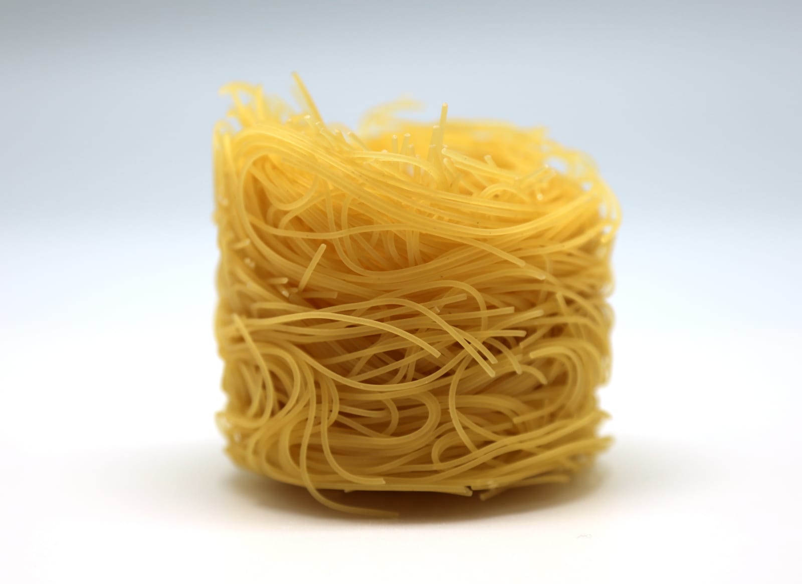 A close stack of very fine dried capelli d’angelo pasta nests on a white surface.