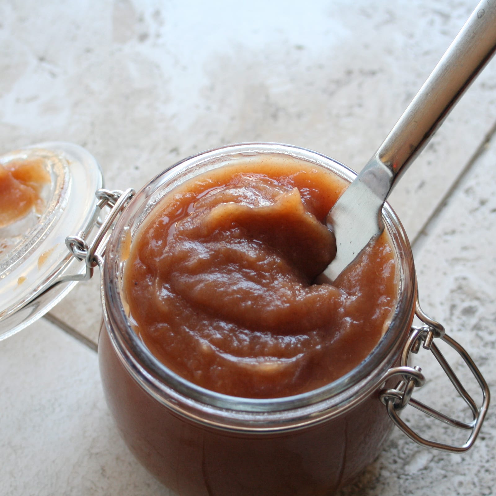 Dark amber apple butter in a glass jar beside fresh red apples.