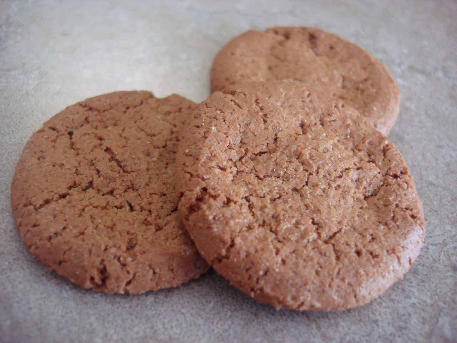 Three round, crackled gingersnap cookies on a pale counter.