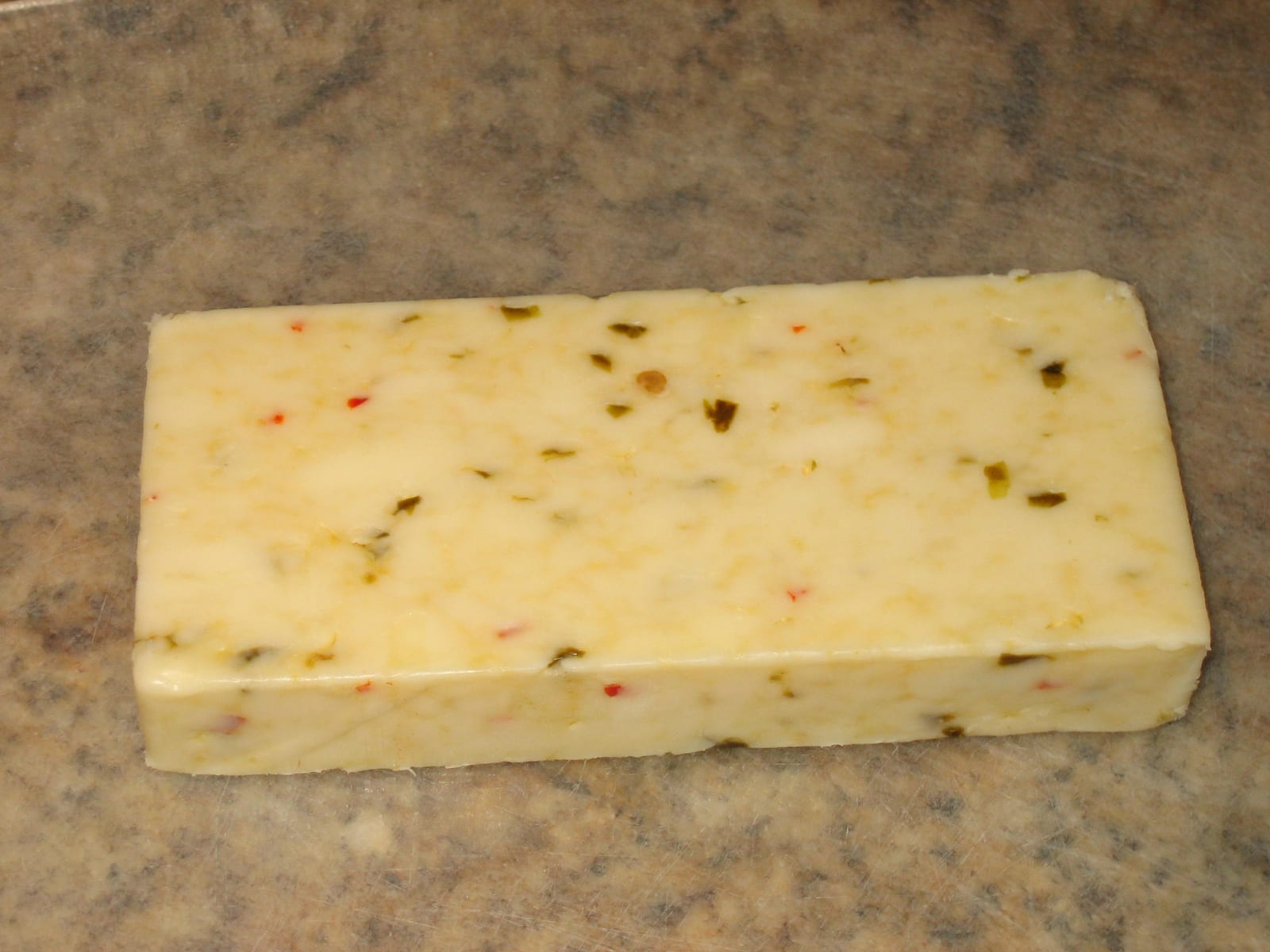 A pale block of pepper Jack cheese dotted with red and green pepper pieces.