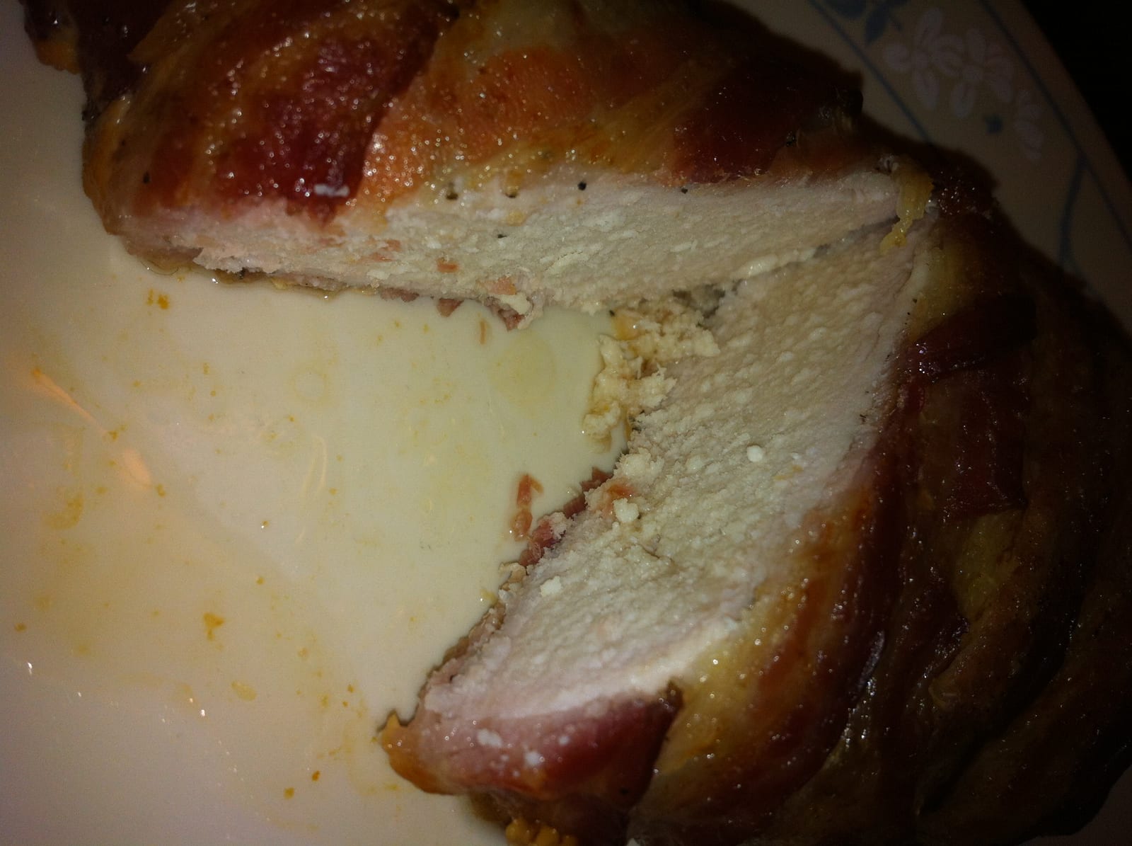 A bacon-wrapped chicken breast sliced across the middle on a patterned plate.