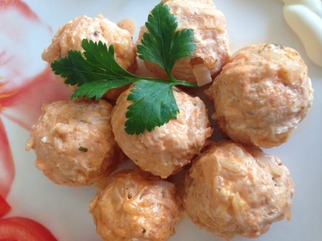 A plate of pale meatballs flecked with rice and garnished with parsley.