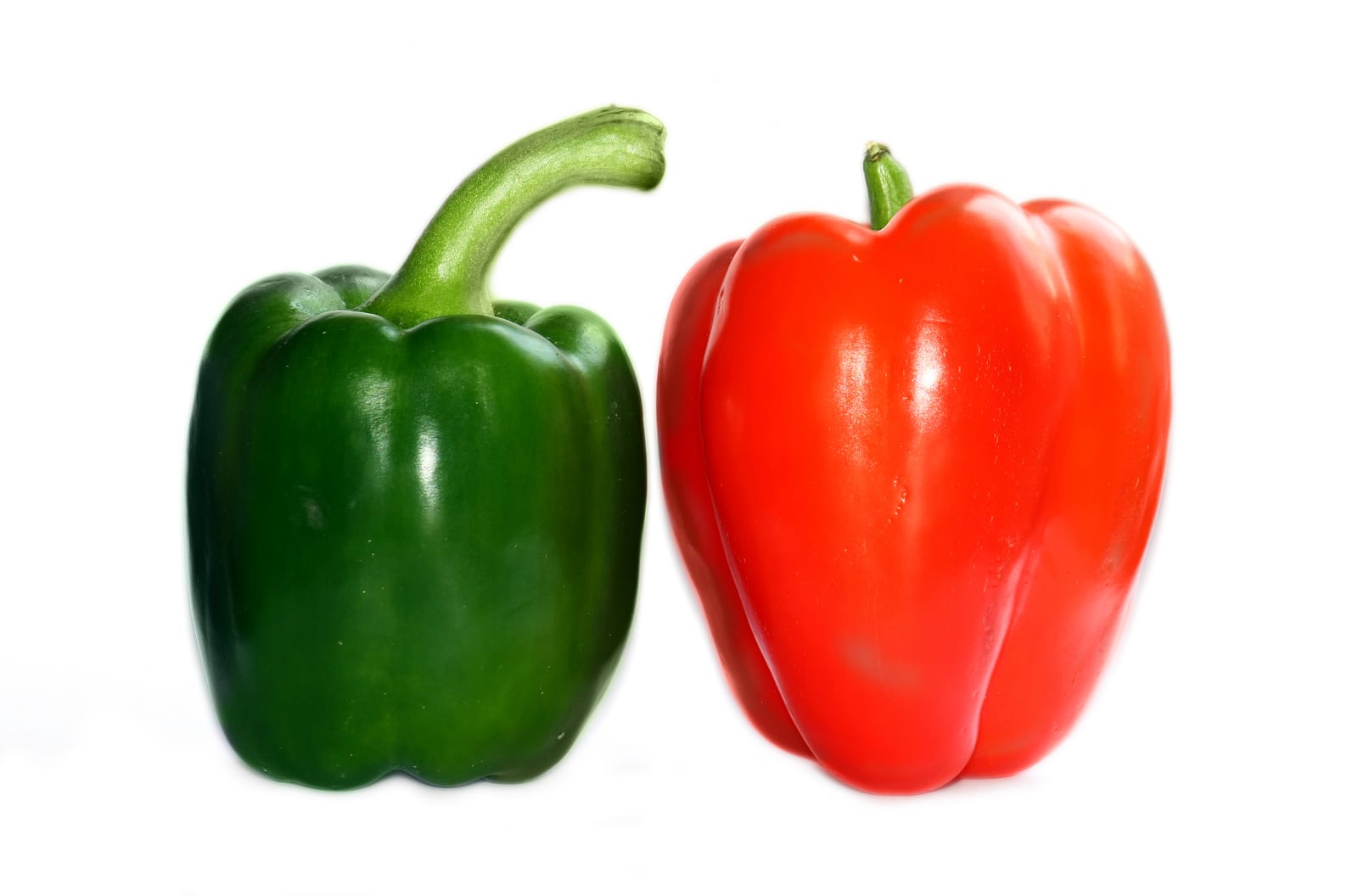 Glossy red and green bell peppers arranged against a pale background.