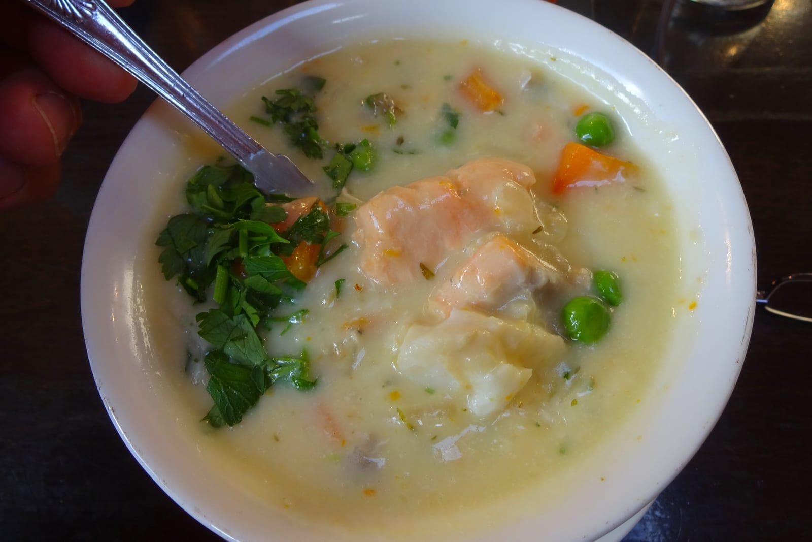 A close view of a creamy seafood chowder with fish, vegetables and parsley.