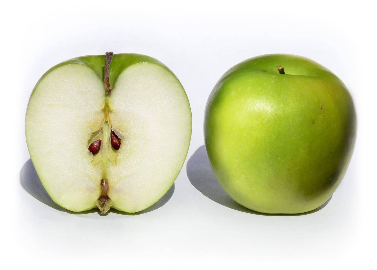 A whole Granny Smith apple beside a halved apple showing pale flesh, core, and seeds.