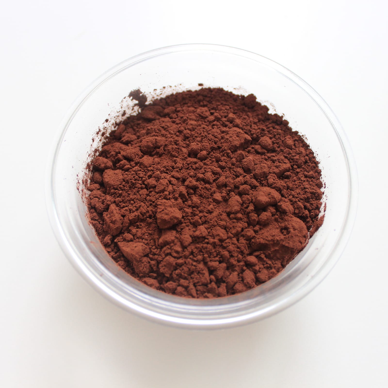 A clear glass bowl filled with deep brown cocoa powder on a white surface.