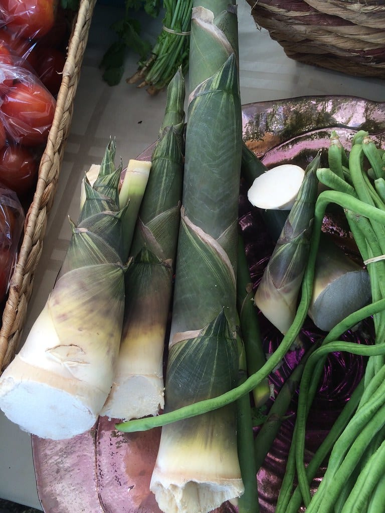 Fresh bamboo shoots with their green husks at a farmers market.