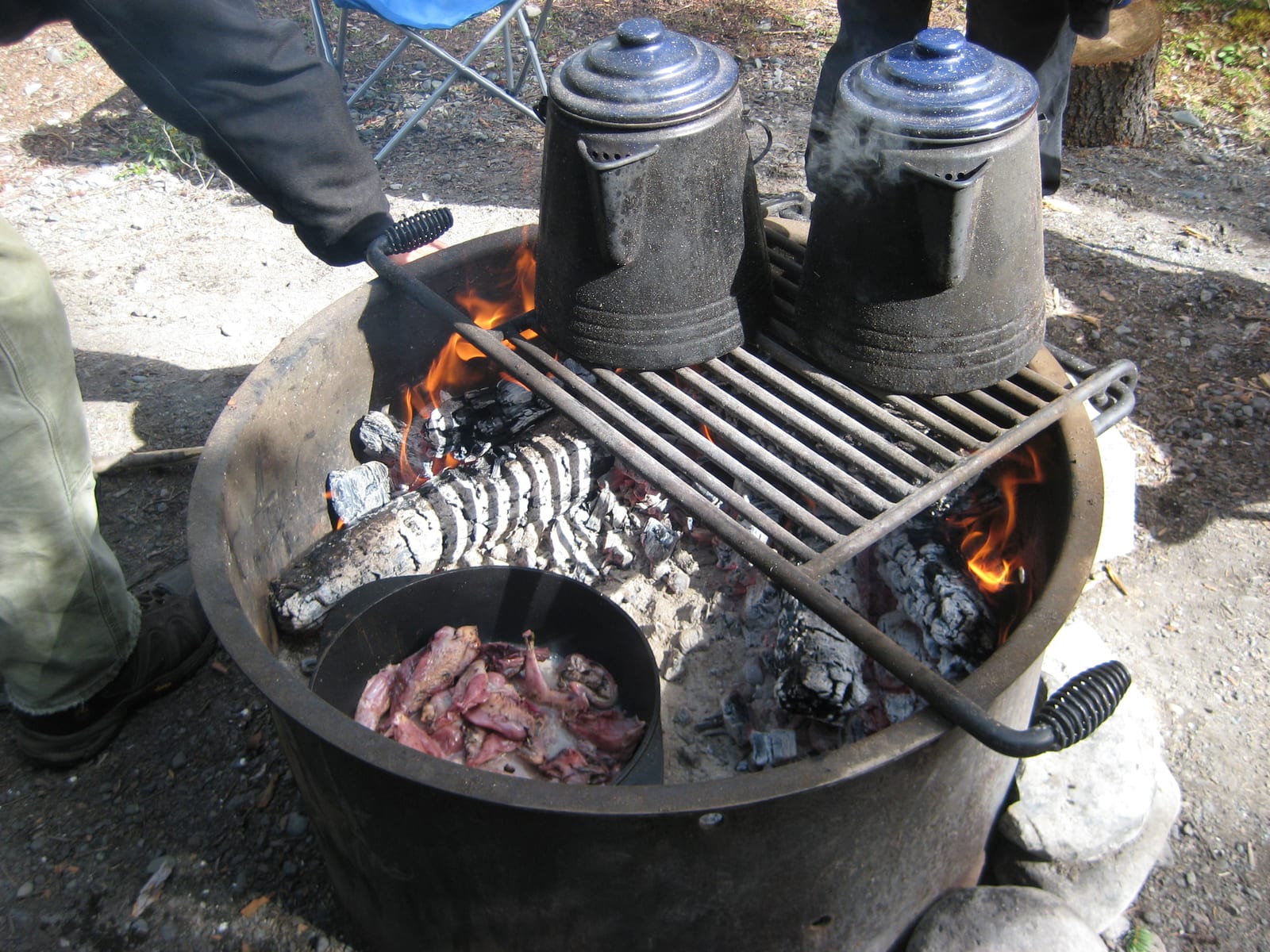 A skillet and kettle resting on a grate above a small campfire.