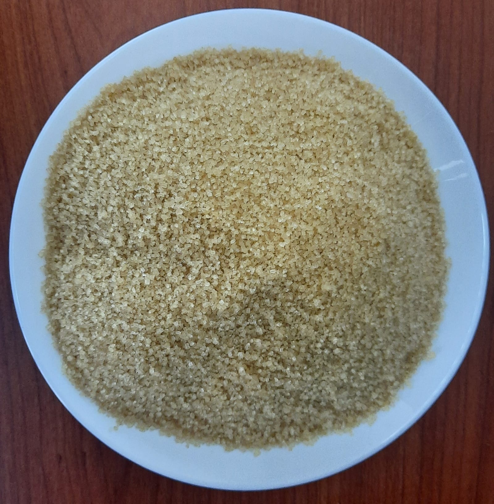 Light brown sugar crystals spread across a white bowl.