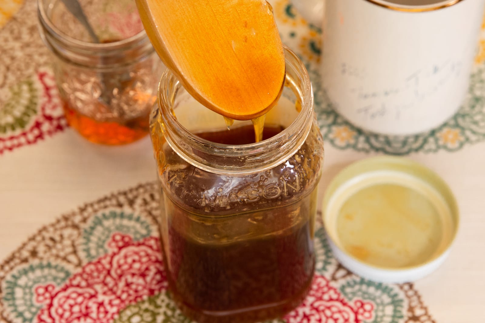 Golden honey dripping from a wooden spoon into a glass jar.