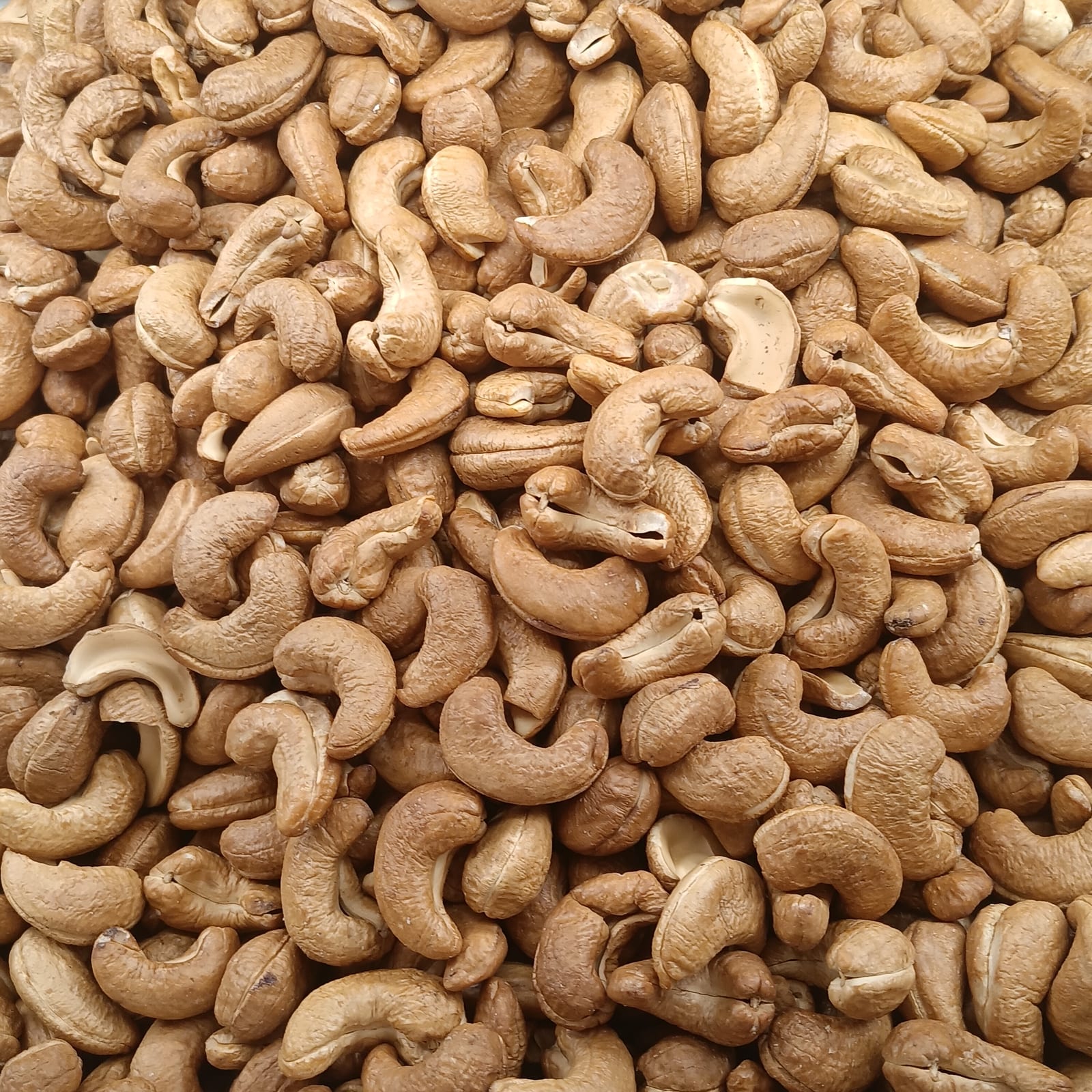 Golden roasted peeled cashews scattered across a dark surface.