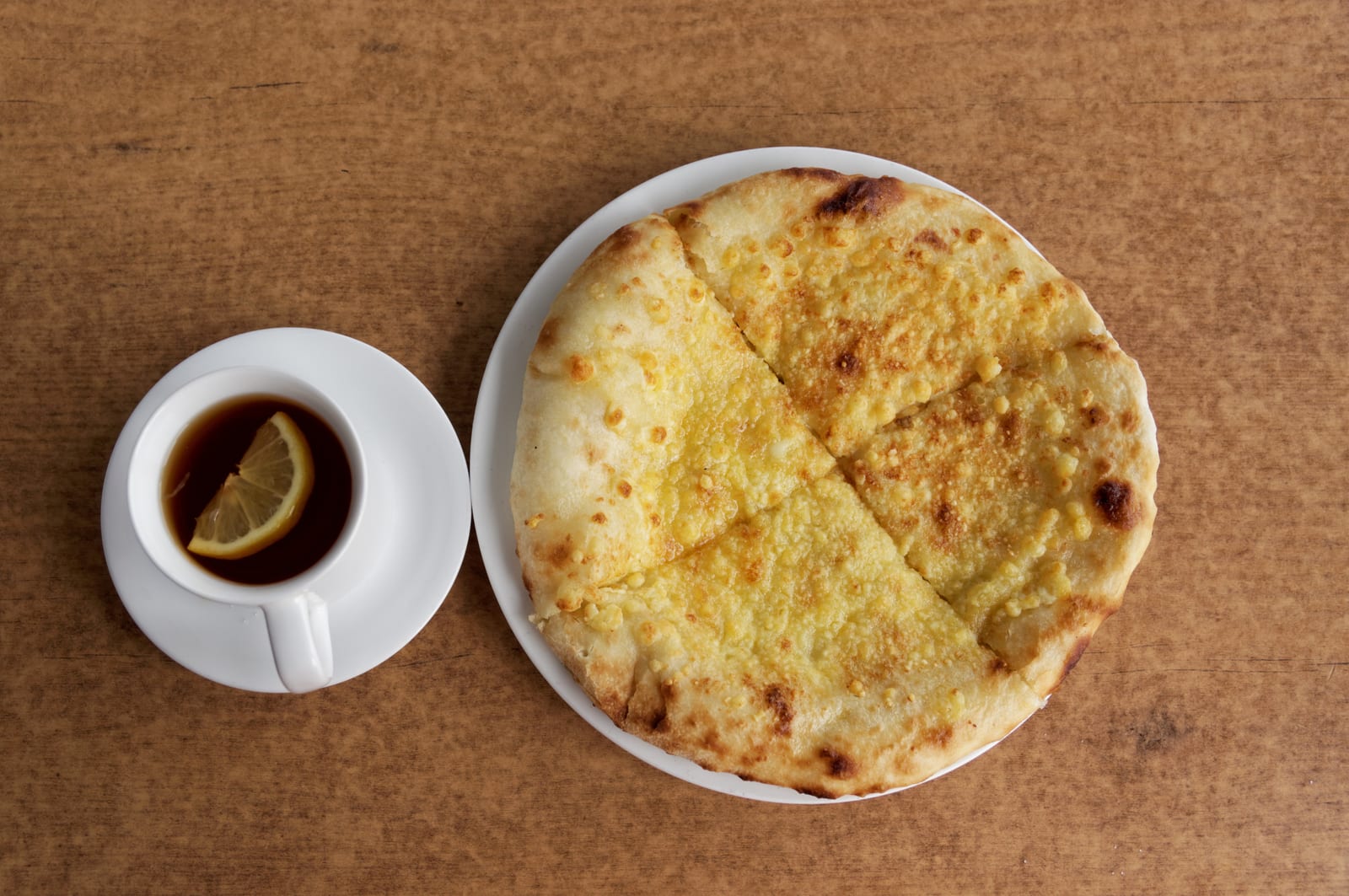 Round Georgian khachapuri on a table with tea and small dishes.