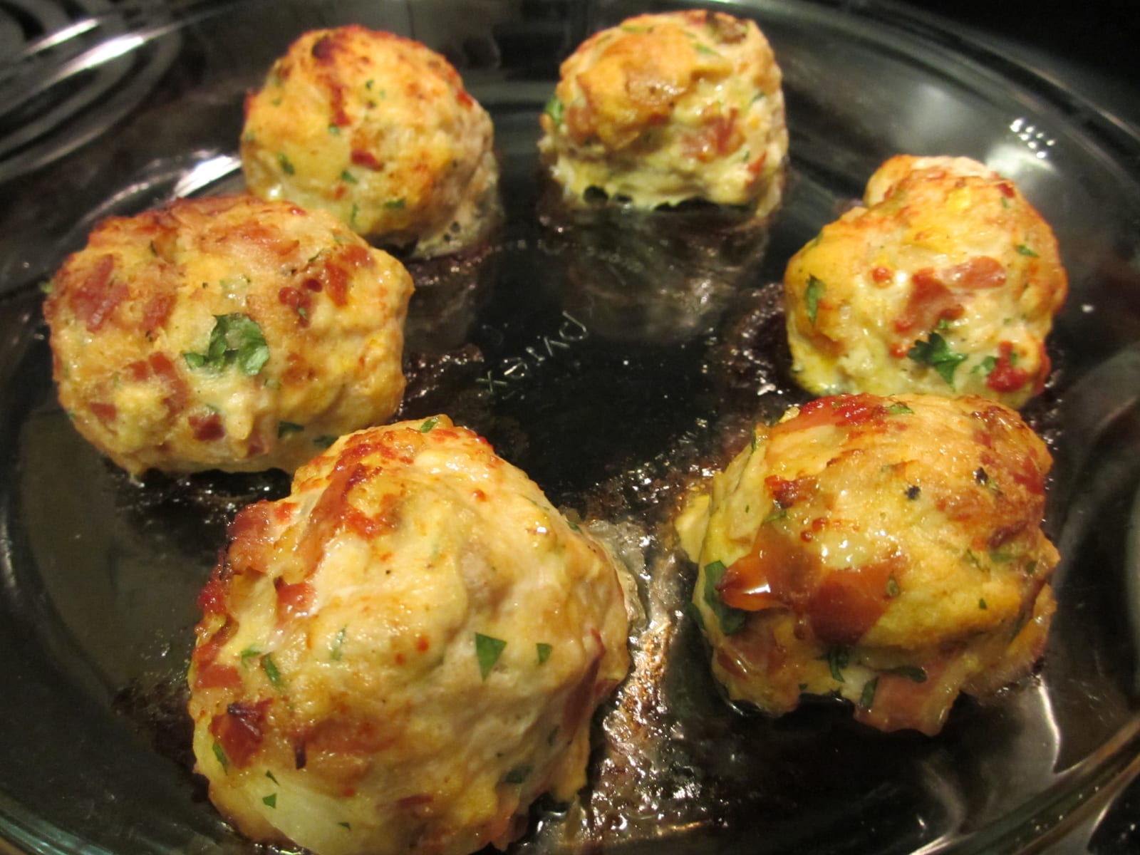 Golden baked chicken meatballs in a skillet, flecked with herbs and tomato.