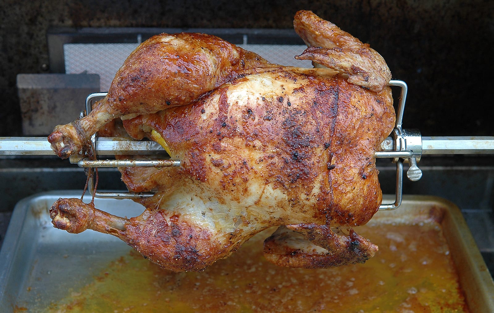 A deeply browned whole chicken turning on a rotisserie spit.