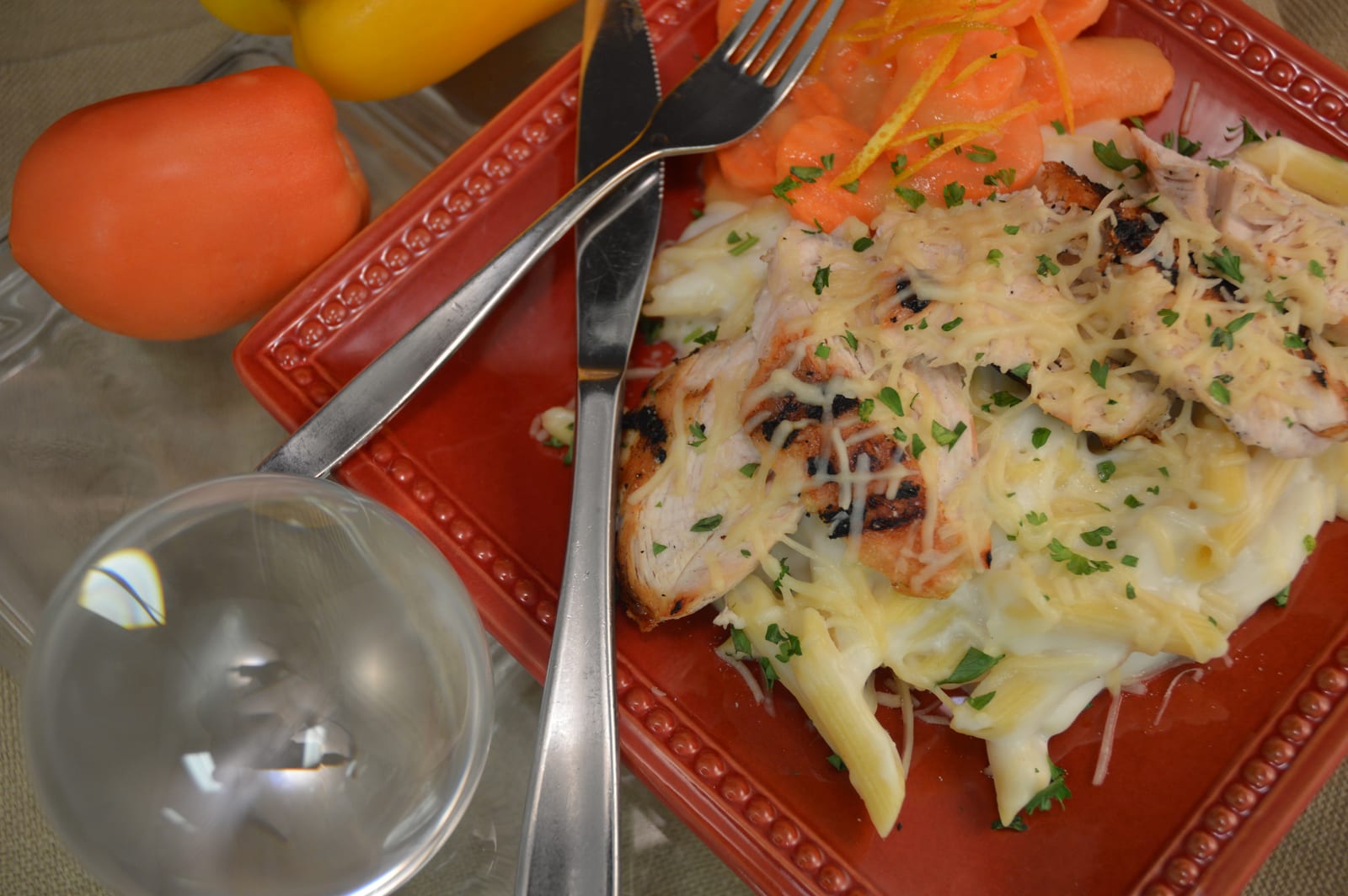 Grilled chicken sliced over creamy Alfredo pasta on a red ceramic plate.