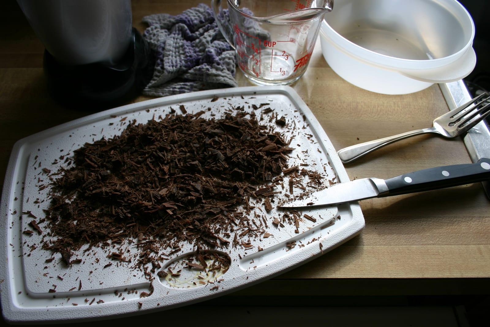 A mound of freshly shaved dark chocolate on a cutting board beside a knife.