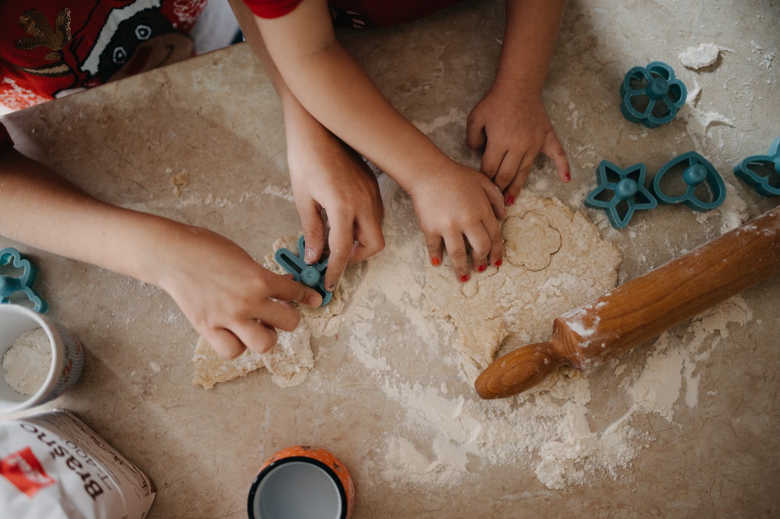 Children’s hands pressing small cookie cutters into rolled dough on a flour-dusted counter.