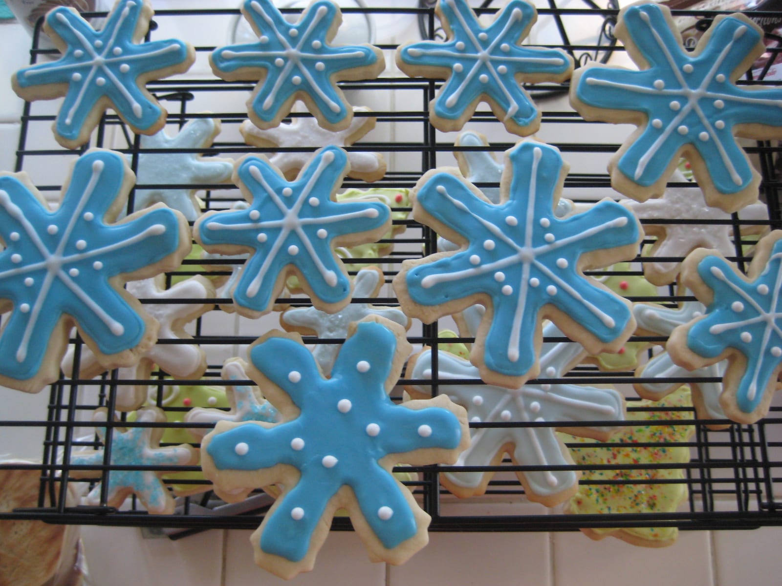 Blue and white royal-iced snowflake sugar cookies cooling on wire racks.