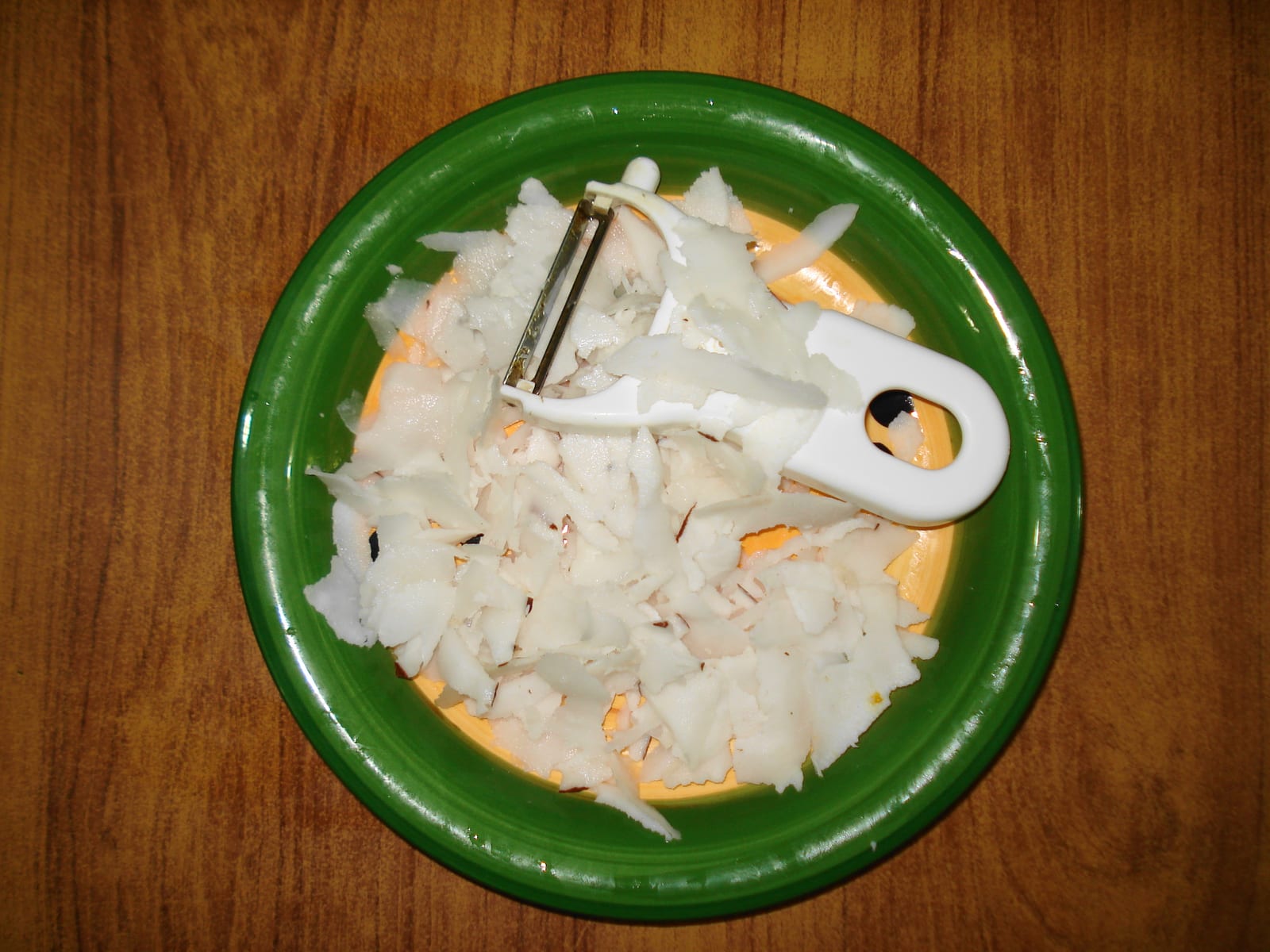Fresh white coconut flakes on a green plate beside a vegetable peeler.