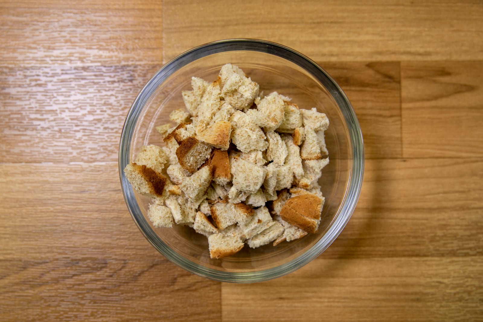 Small pieces of bread in a clear bowl on a wooden work surface.