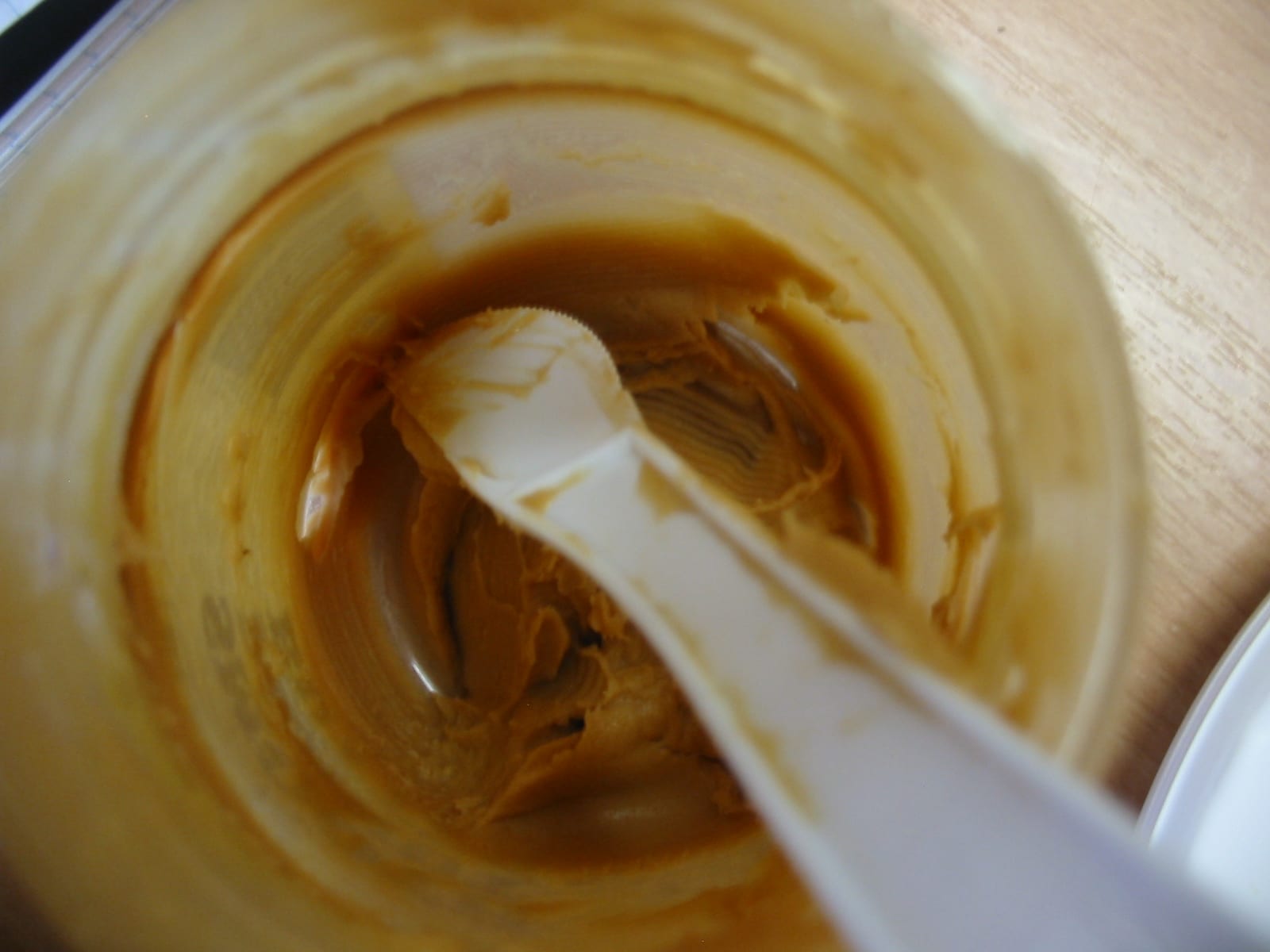 A white plastic knife resting inside a nearly empty jar streaked with creamy peanut butter.