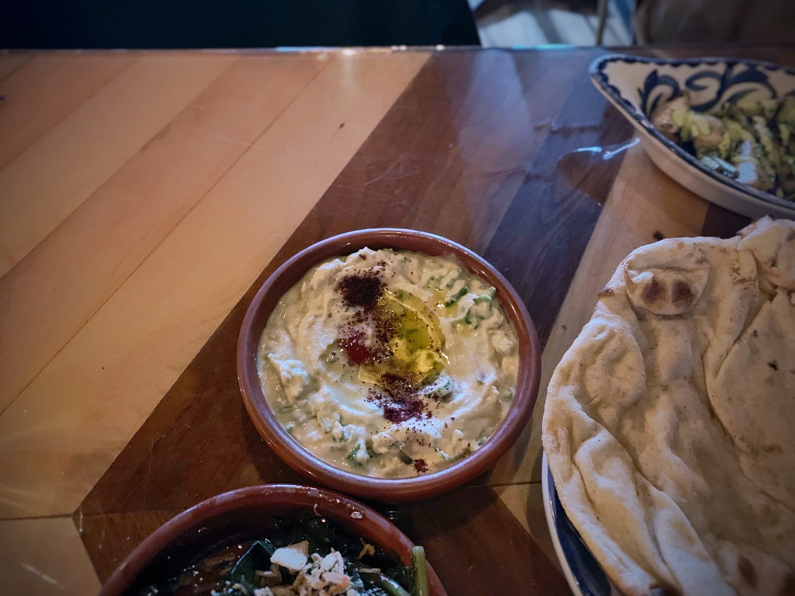 Restaurant hummus with olive oil, chickpeas, lemon, and pieces of flatbread on a wooden table.