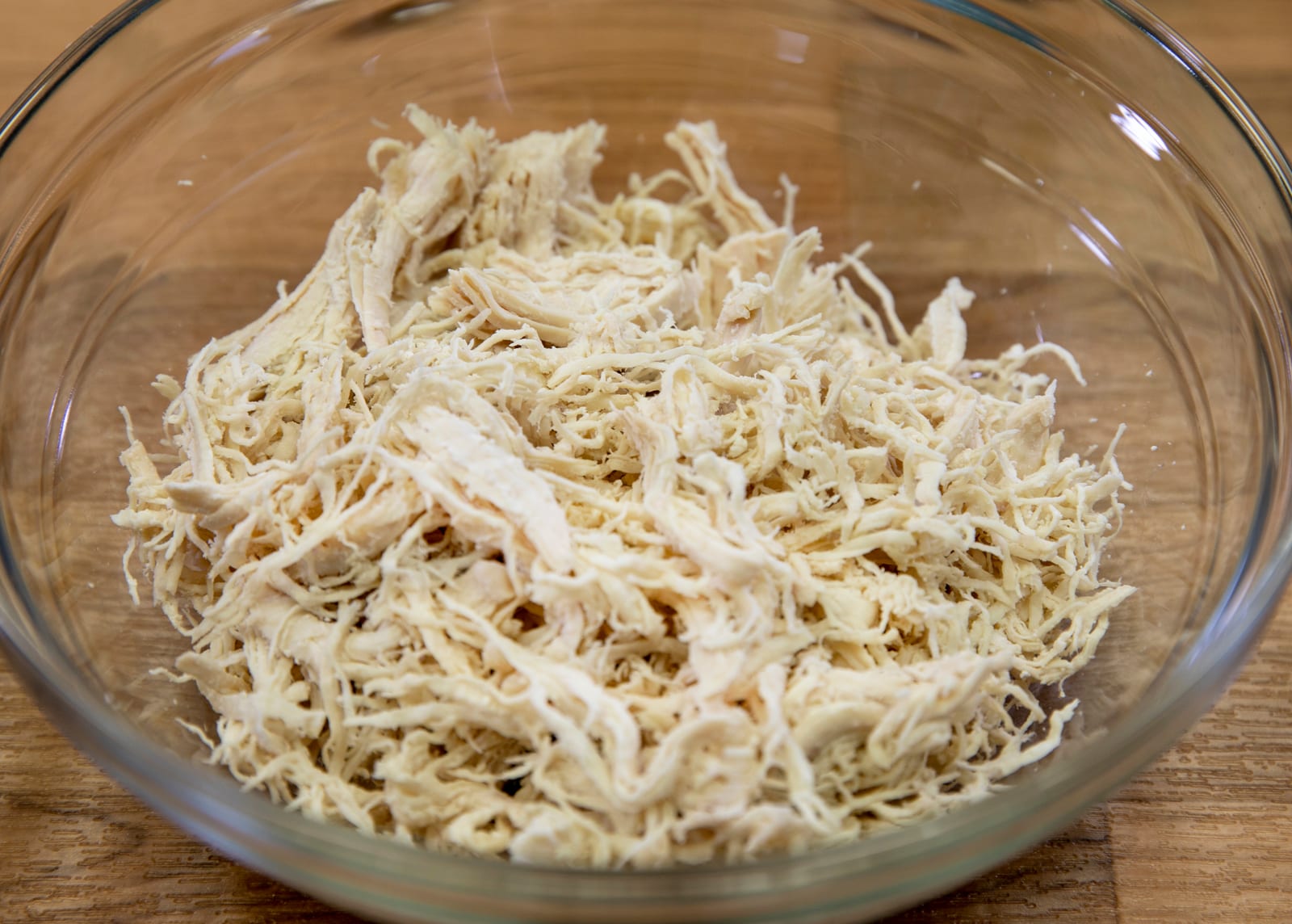 A clear glass bowl filled with cooked shredded white-meat chicken.