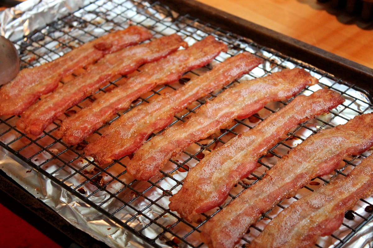 Several browned strips of cooked bacon on a white plate.
