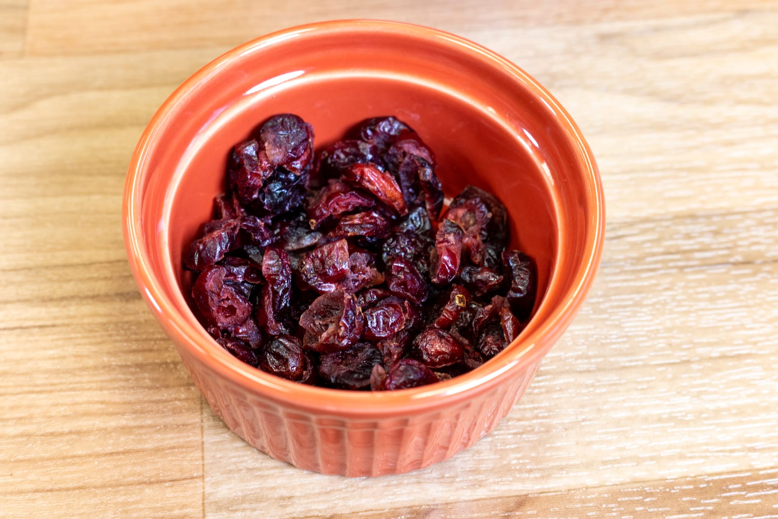 Deep red dried cranberries in a small orange ceramic bowl.