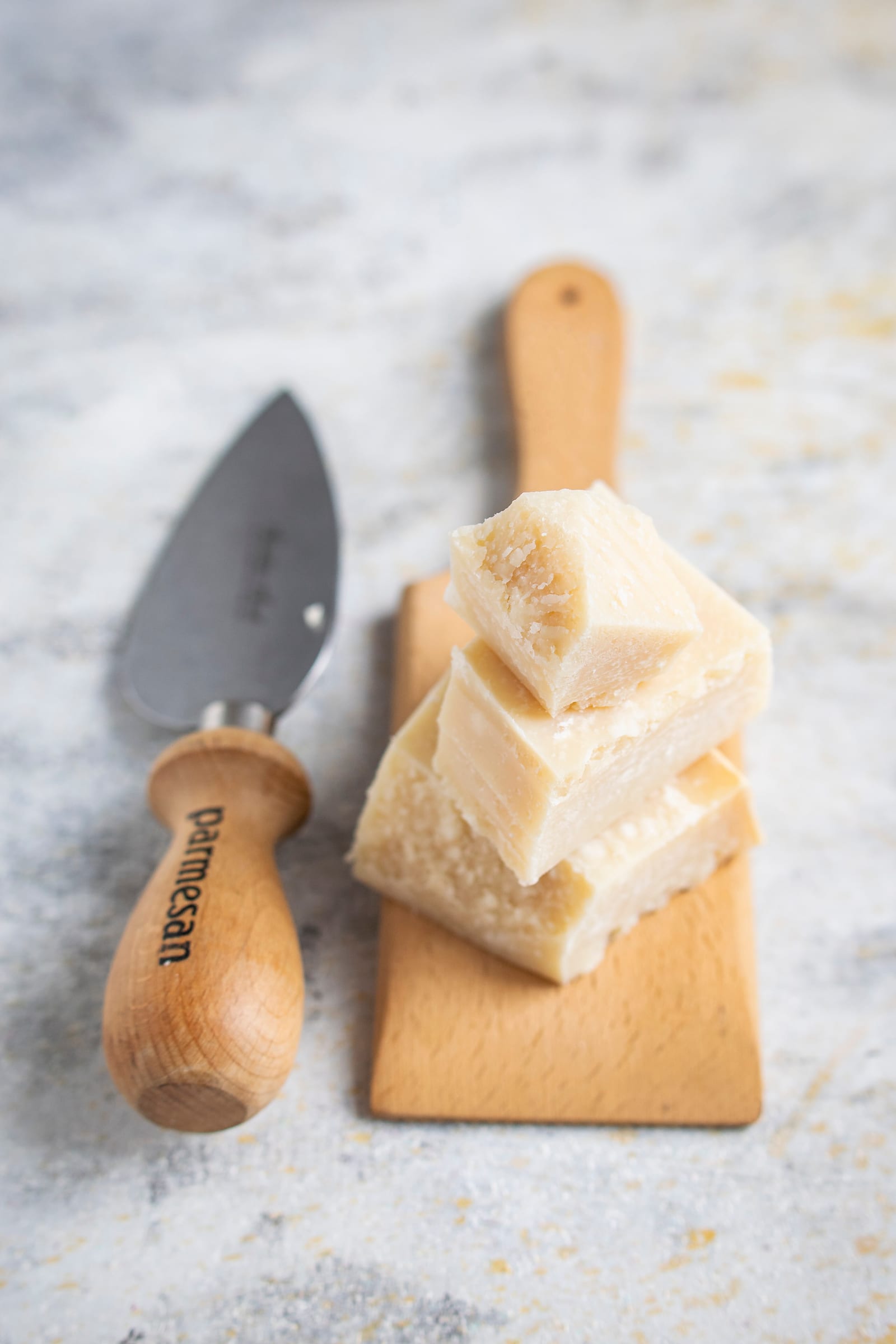 Pale blocks of Parmesan stacked beside a wooden-handled cheese knife.