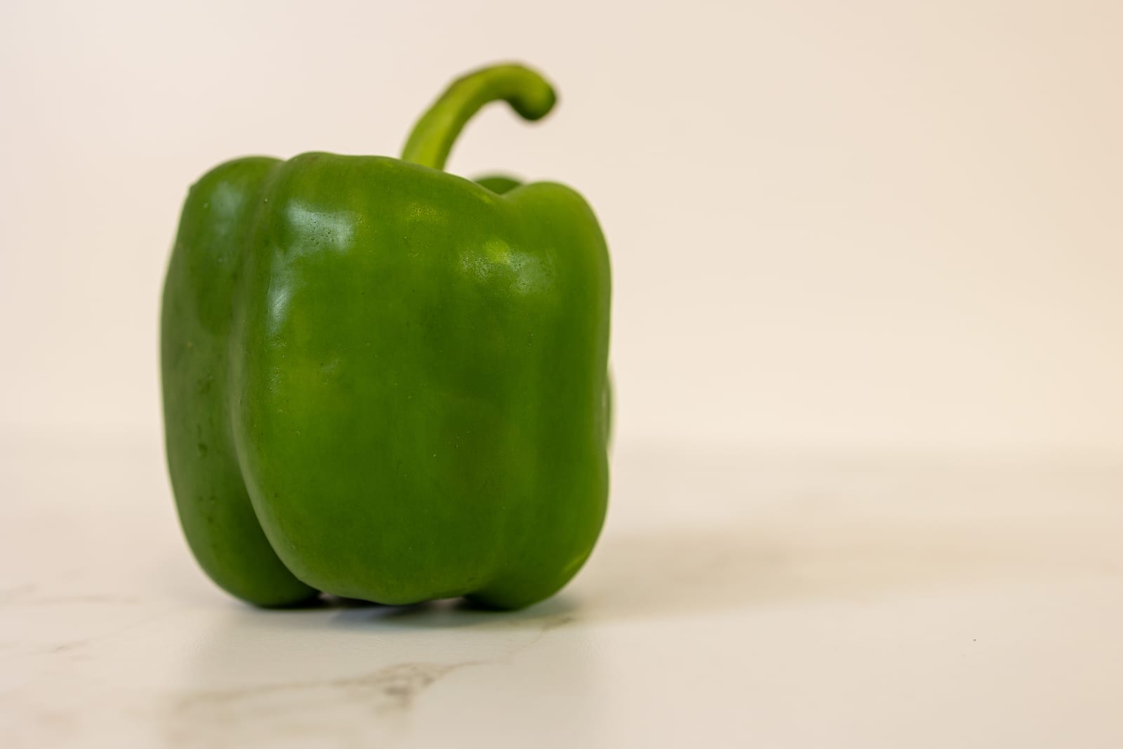 Two whole green bell peppers resting against a softly blurred garden background.