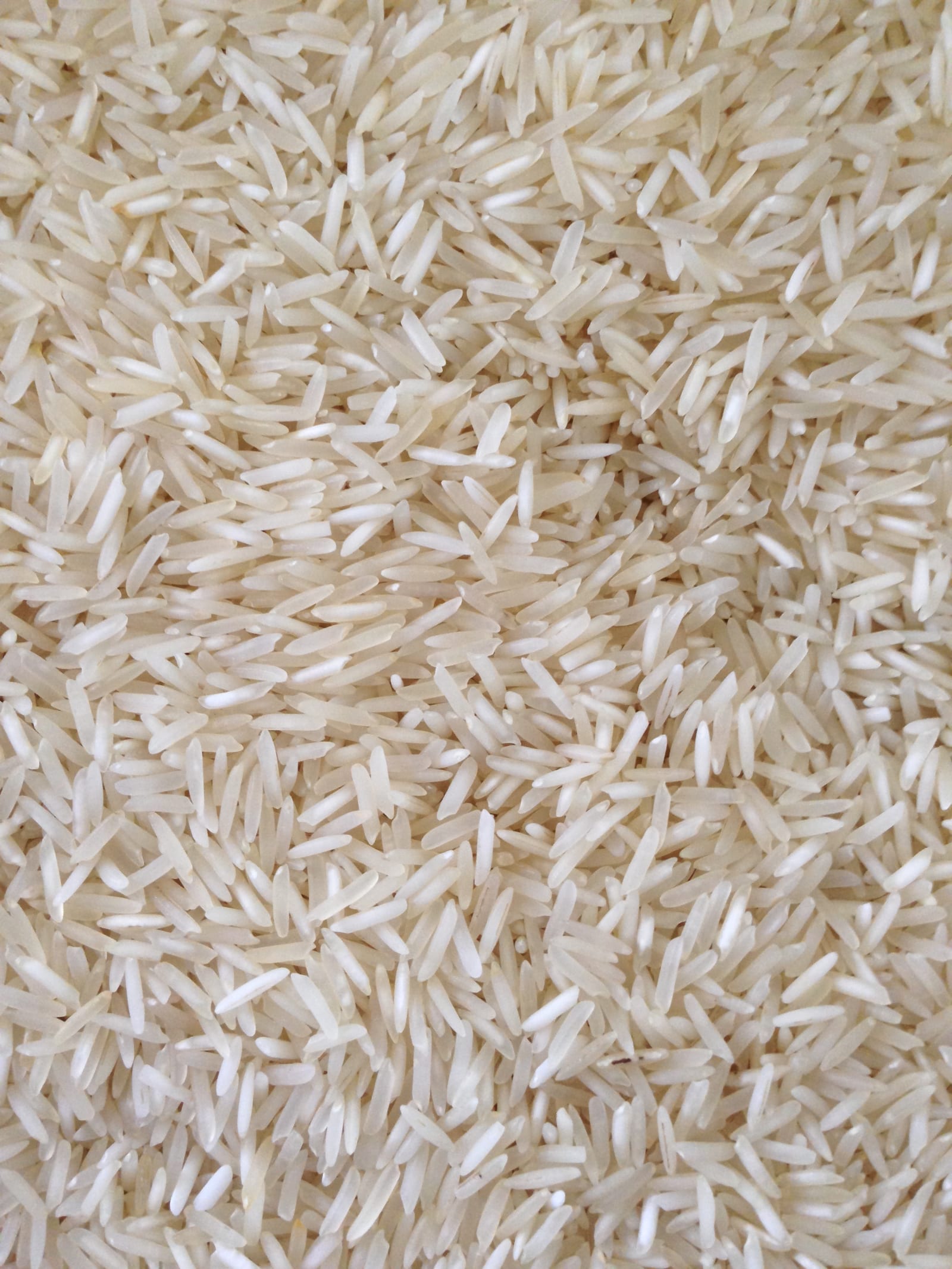 Uncooked long-grain white rice scattered across a wooden surface.
