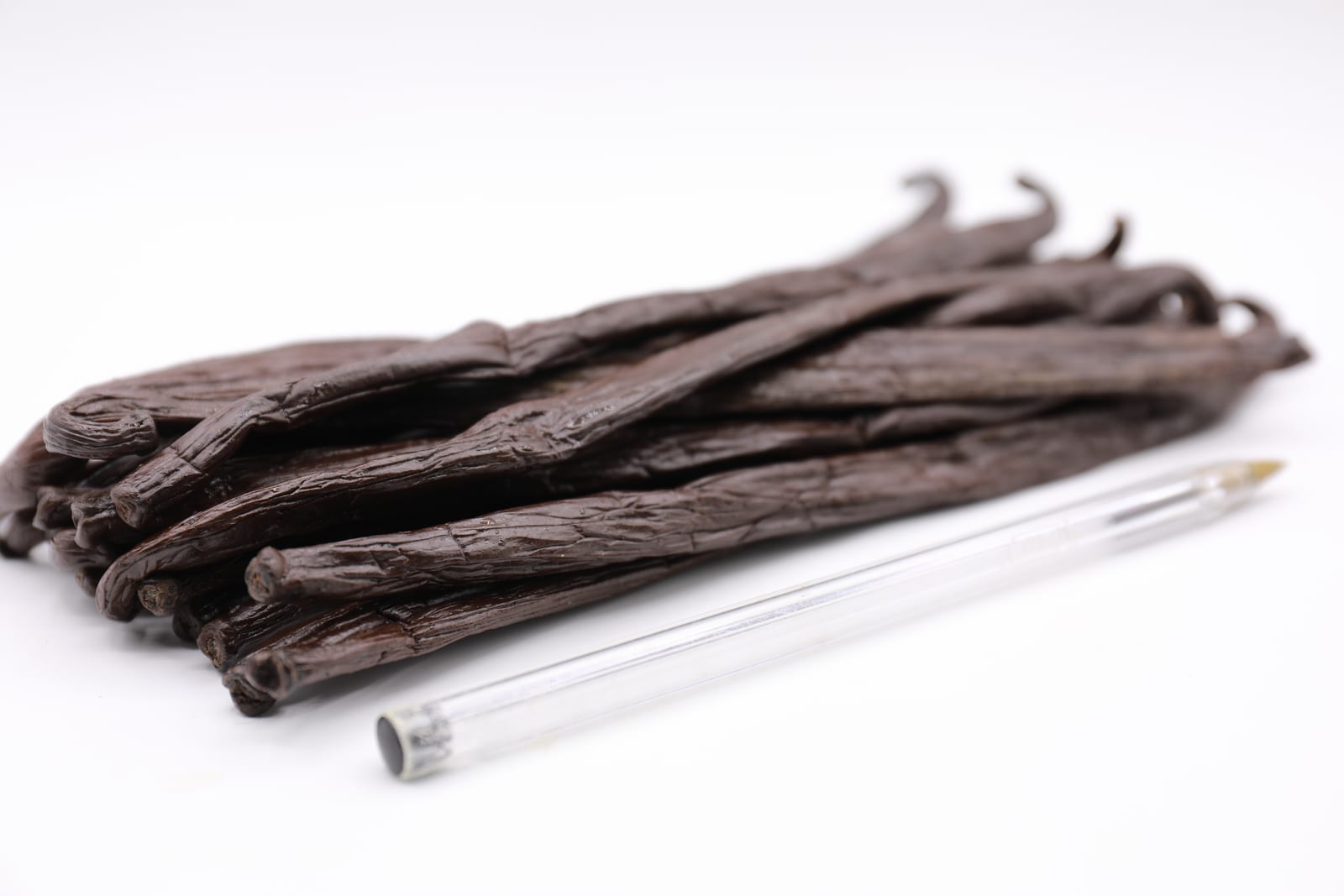 Glossy cured Tahitian vanilla beans laid in parallel rows on a pale wood surface.