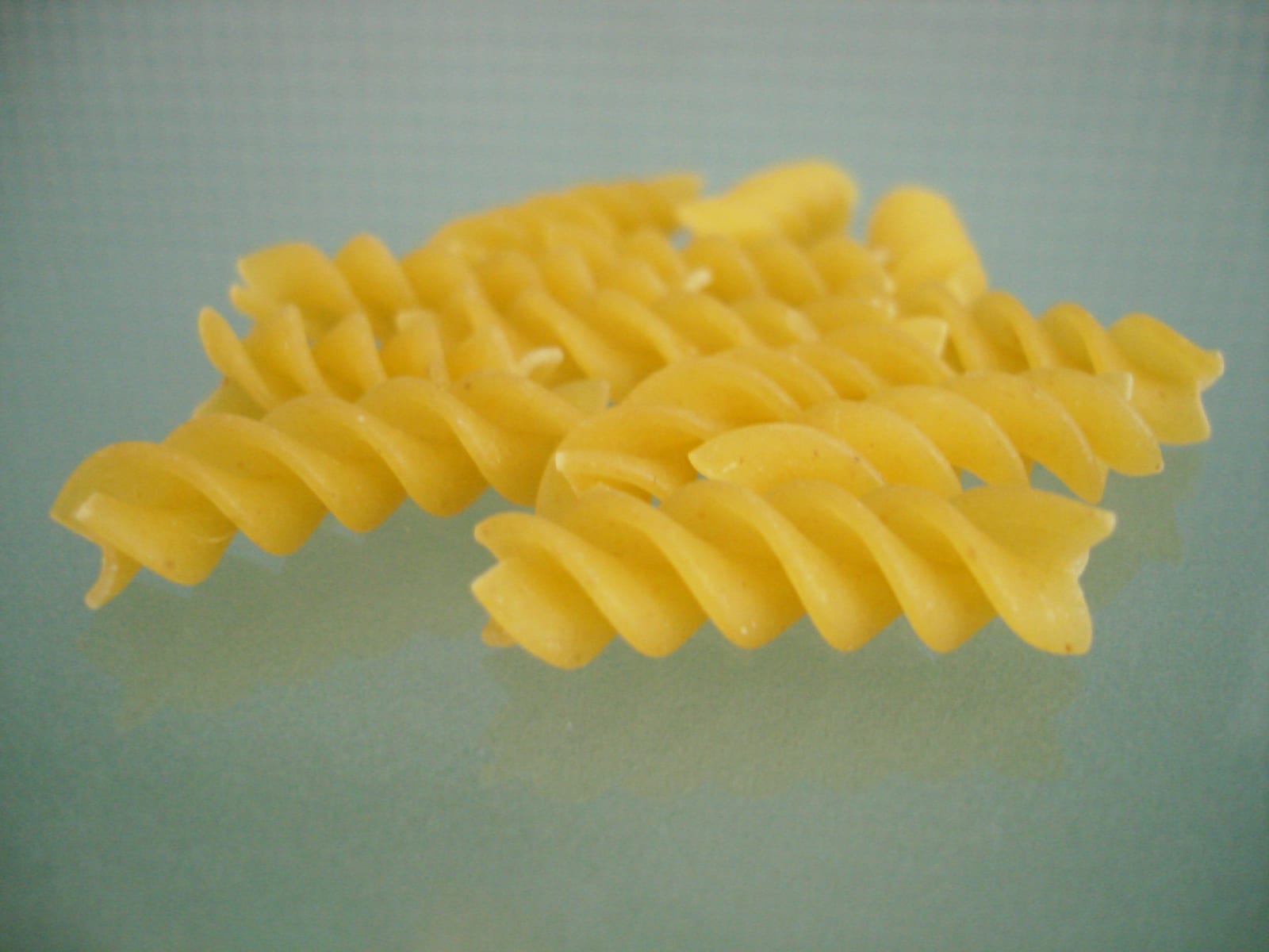 Two pieces of uncooked yellow rotini pasta enlarged against a cool blue background.
