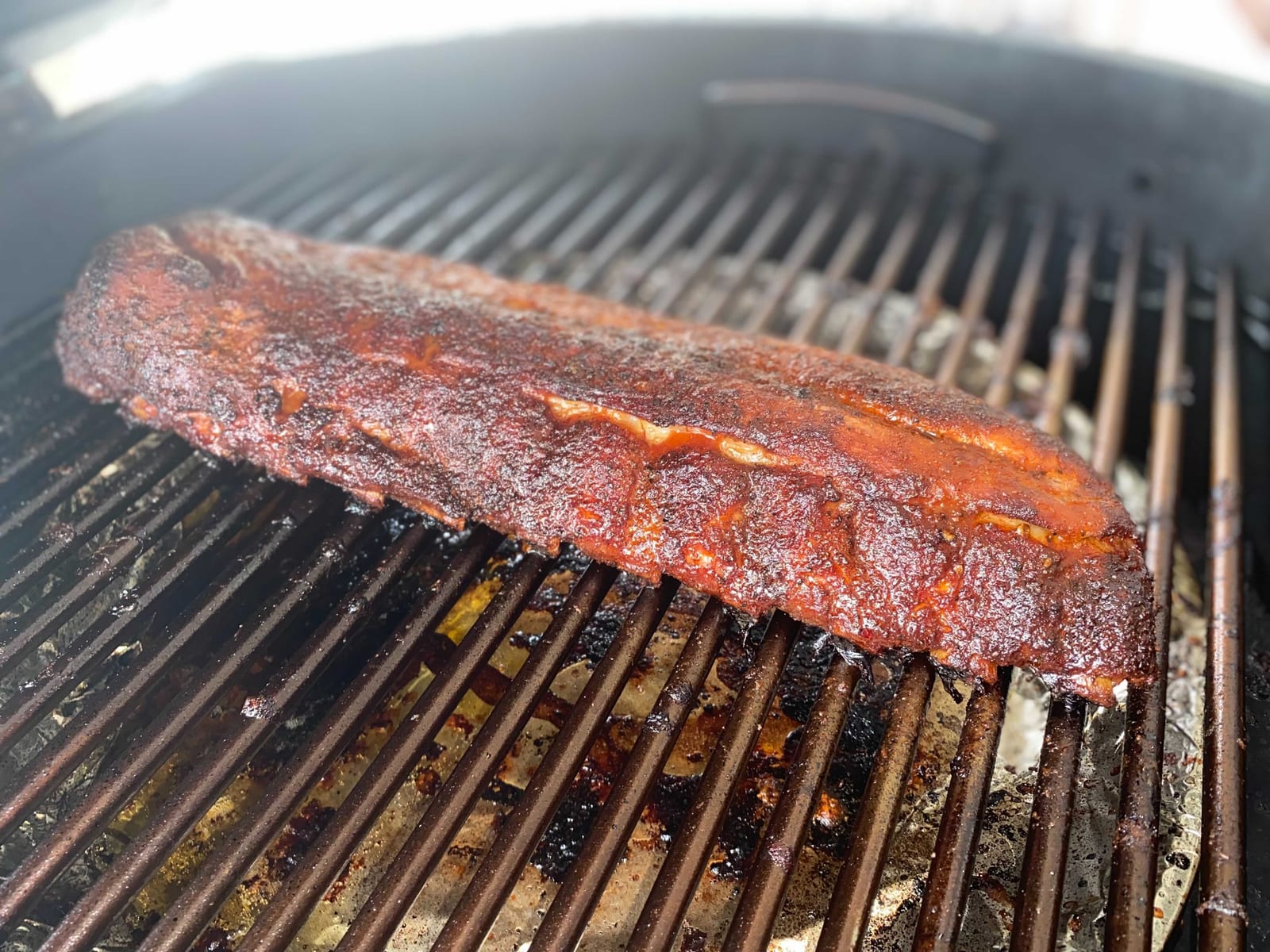A rack of pork ribs glazing over a grill with smoke and bright light around the grate.