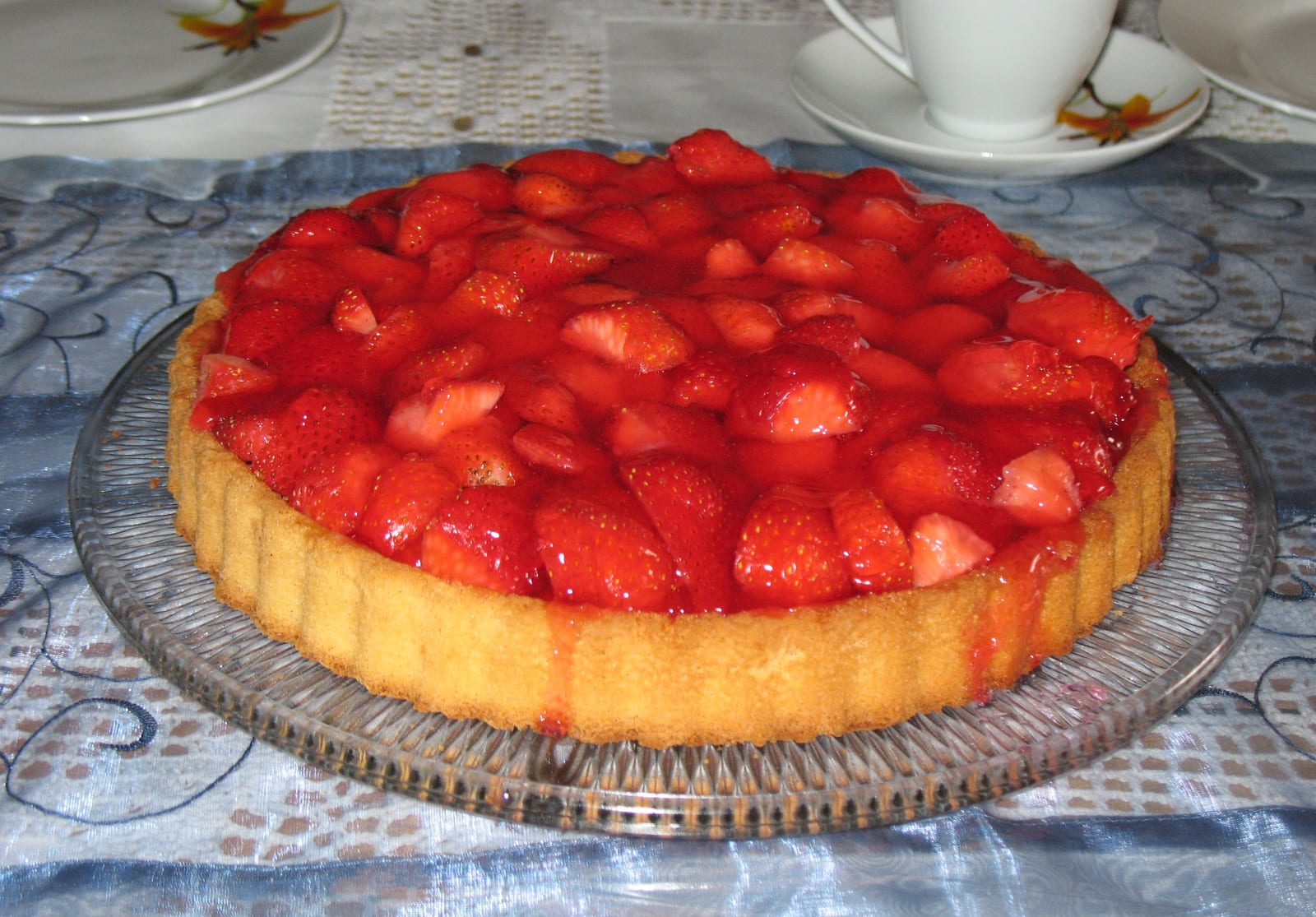 A wide strawberry pie covered with glossy red fruit in a golden crust.
