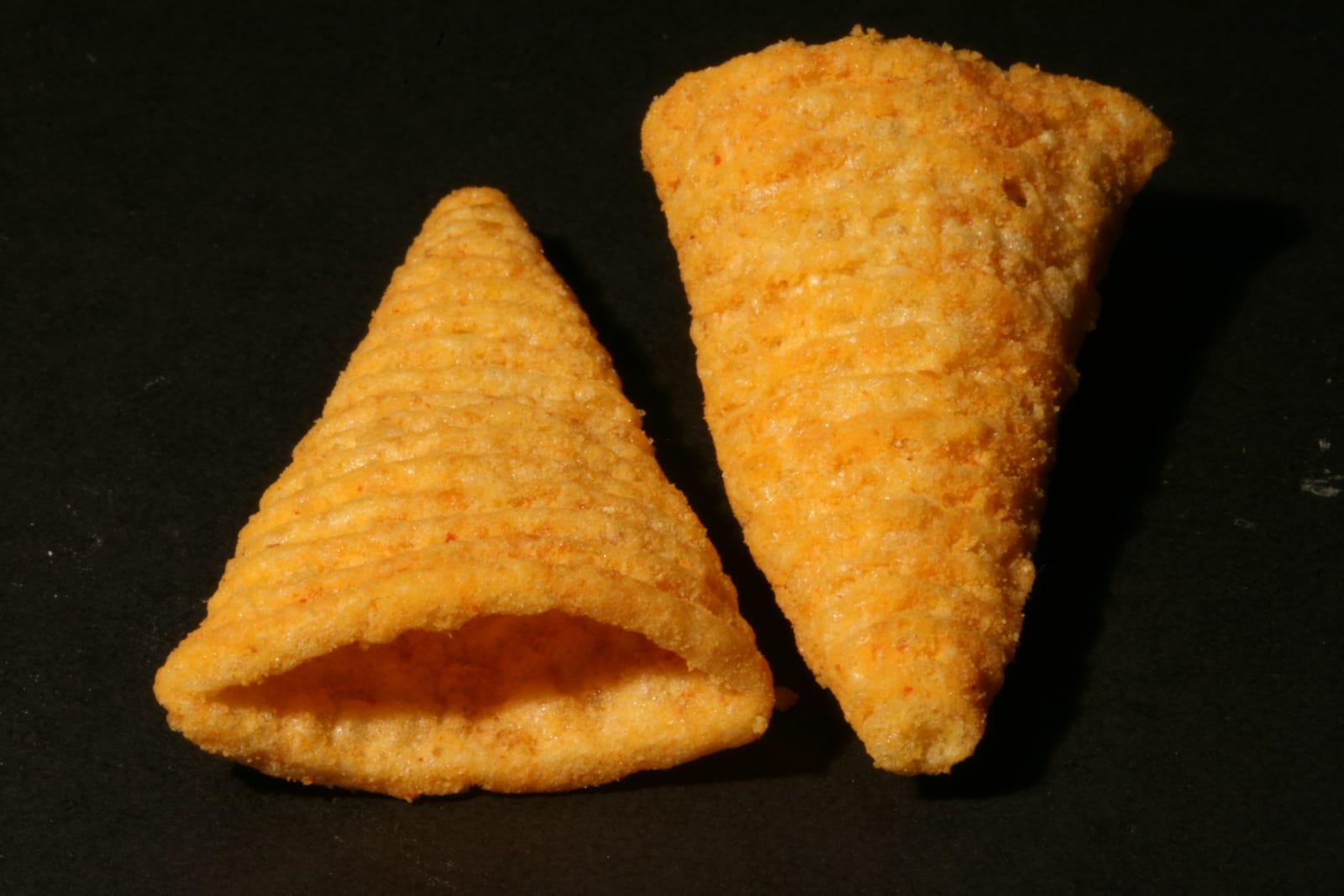 Close-up of golden cone-shaped corn snacks against a black background.