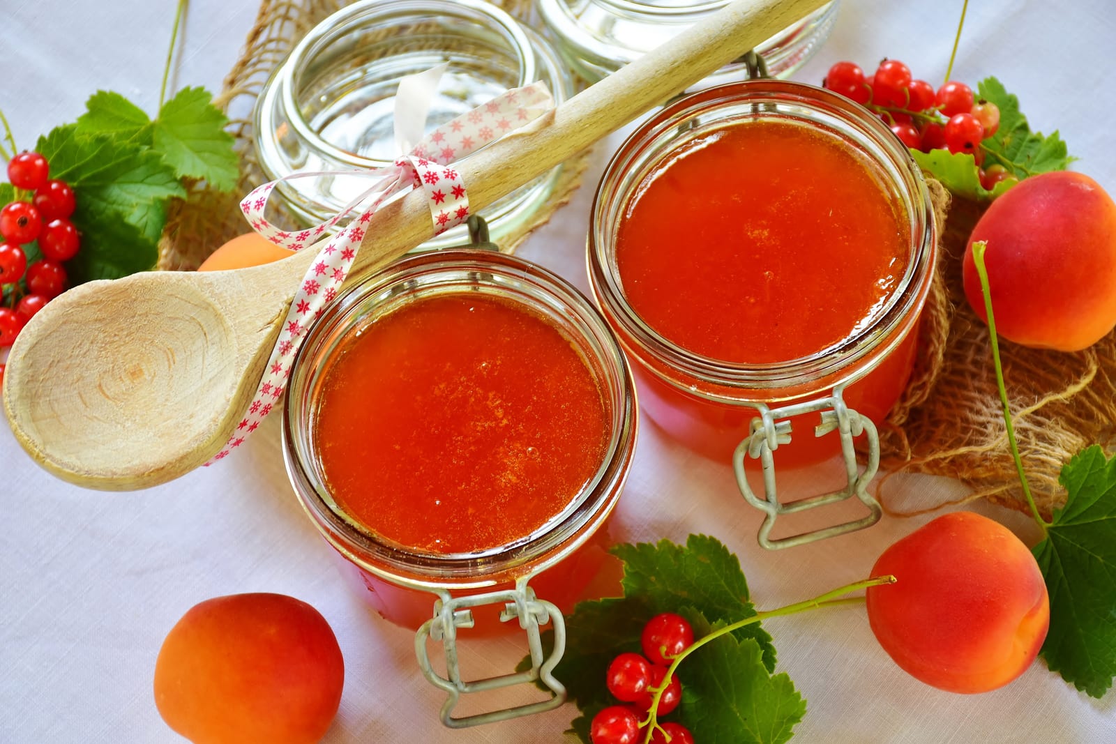 Two open glass jars filled with glossy orange apricot jam beside fresh apricots.