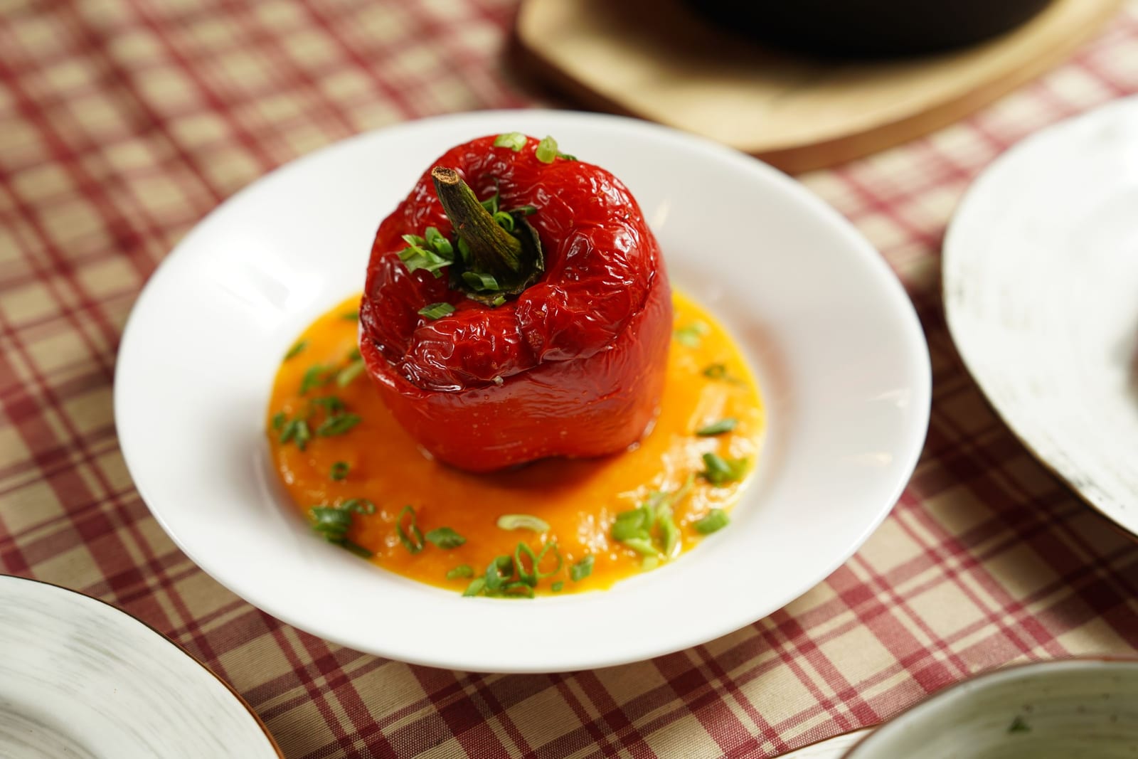 A whole roasted red bell pepper standing in a shallow pool of orange-red sauce on a white plate.