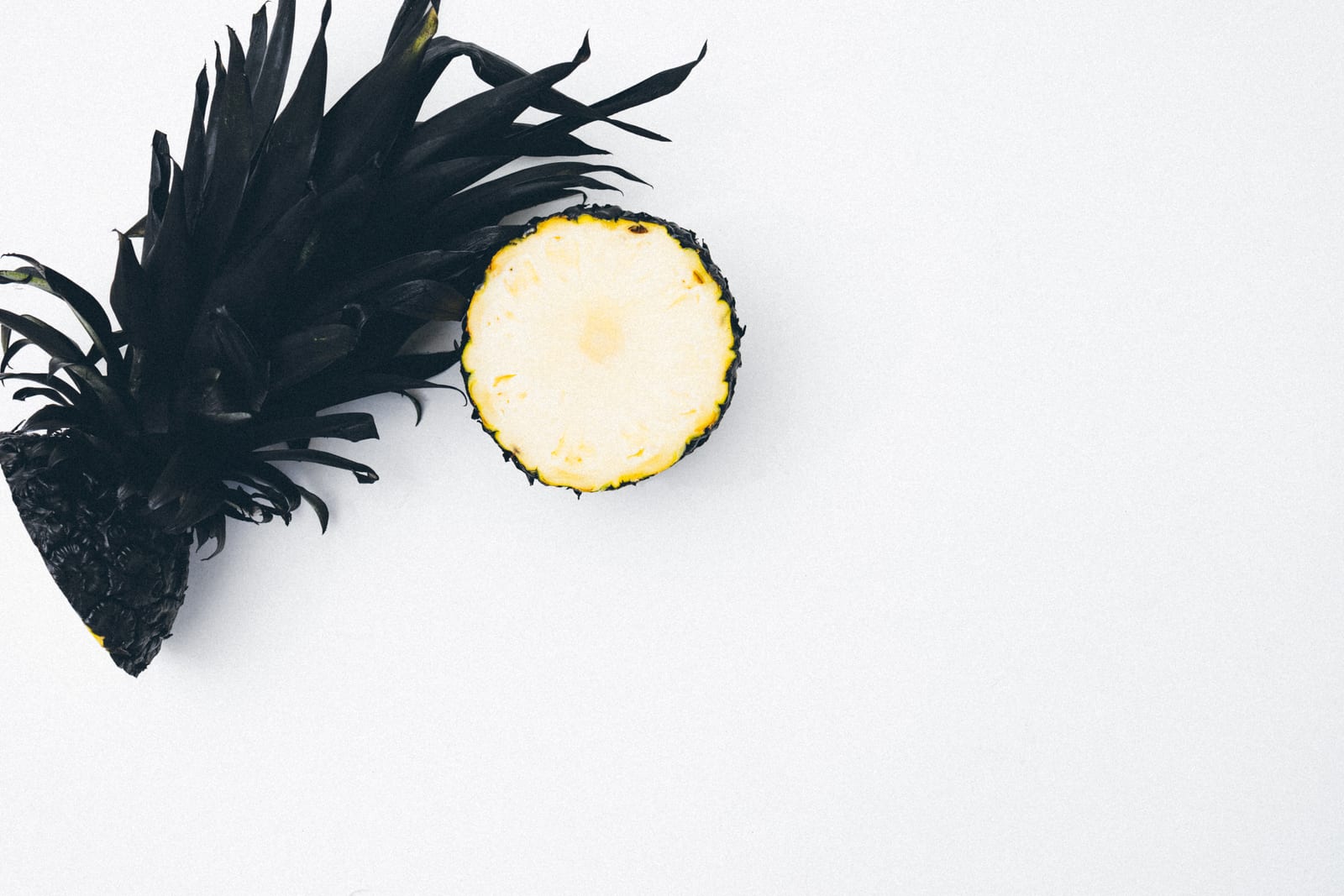 A pineapple split lengthwise and crosswise on a bright white surface.