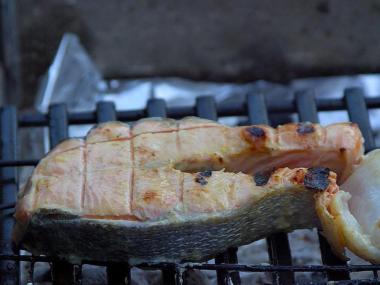 Skin-on salmon steaks cooking directly over dark grill grates.