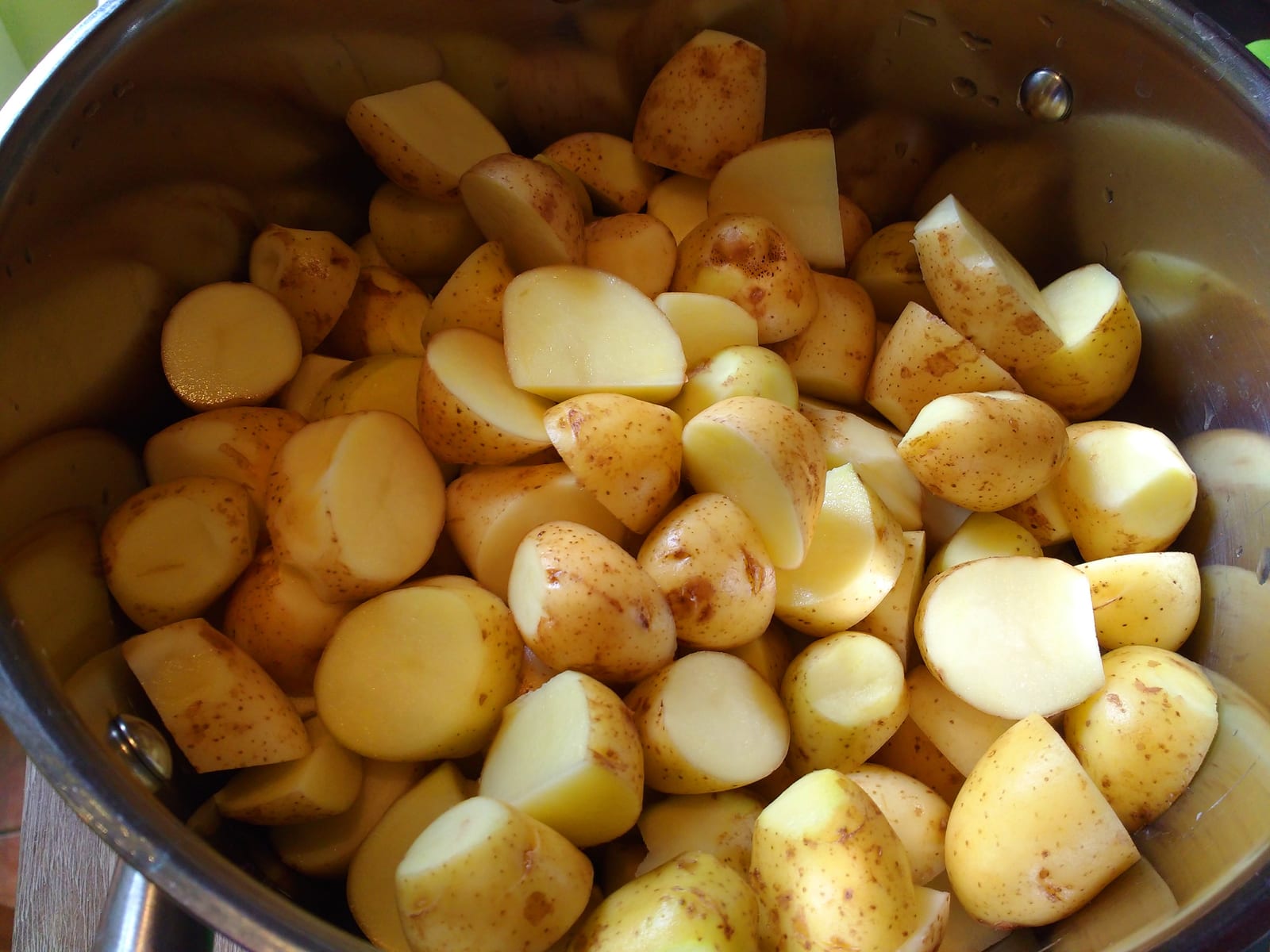 Small yellow potatoes, some halved, gathered in a stainless-steel pot.