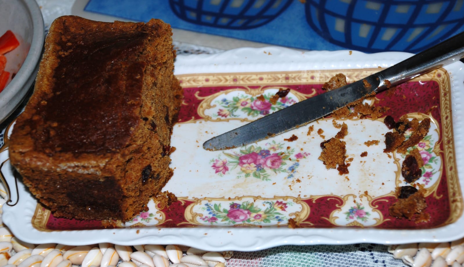 A partly sliced dark pumpkin loaf with visible raisins on an ornate serving platter.