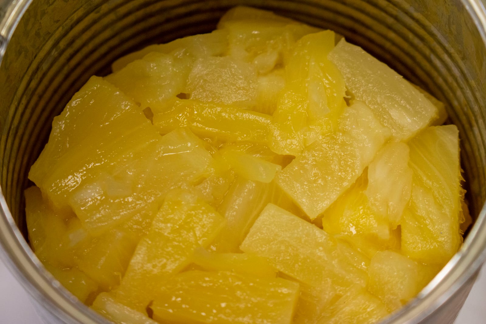 Golden pineapple chunks and juice inside a glass preserving jar.